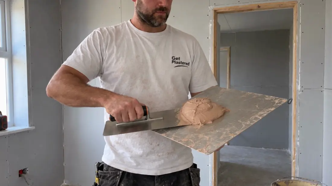 A plasterer smoothing a wall in a stripped back room